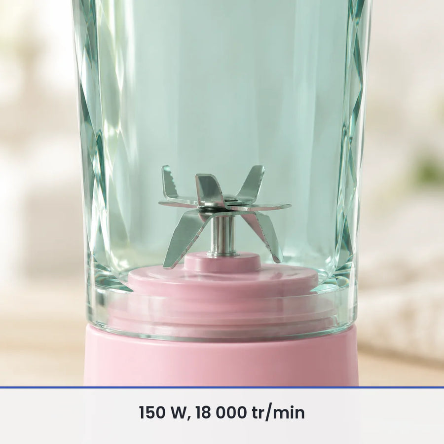 Gros plan sur les lames inox du blender portable rose 600 ml, vues à travers le gobelet vert d'eau transparent