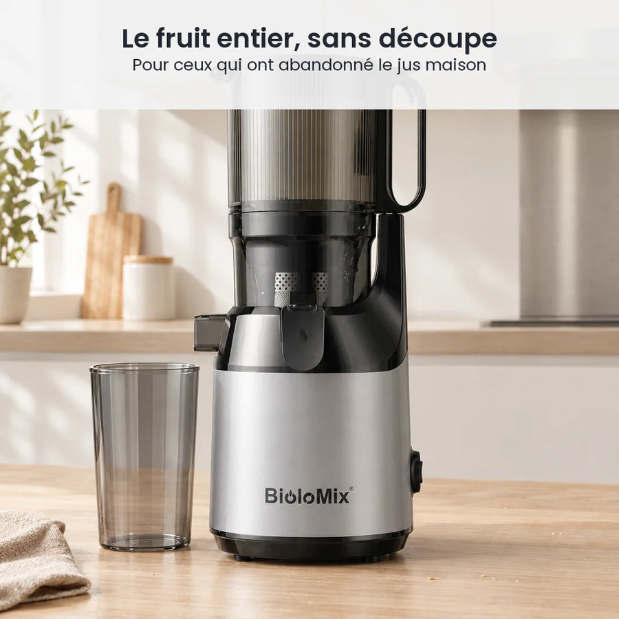 Extracteur de jus BioloMix posé sur le plan de travail d'une cuisine claire, son gobelet à jus transparent fumé à côté