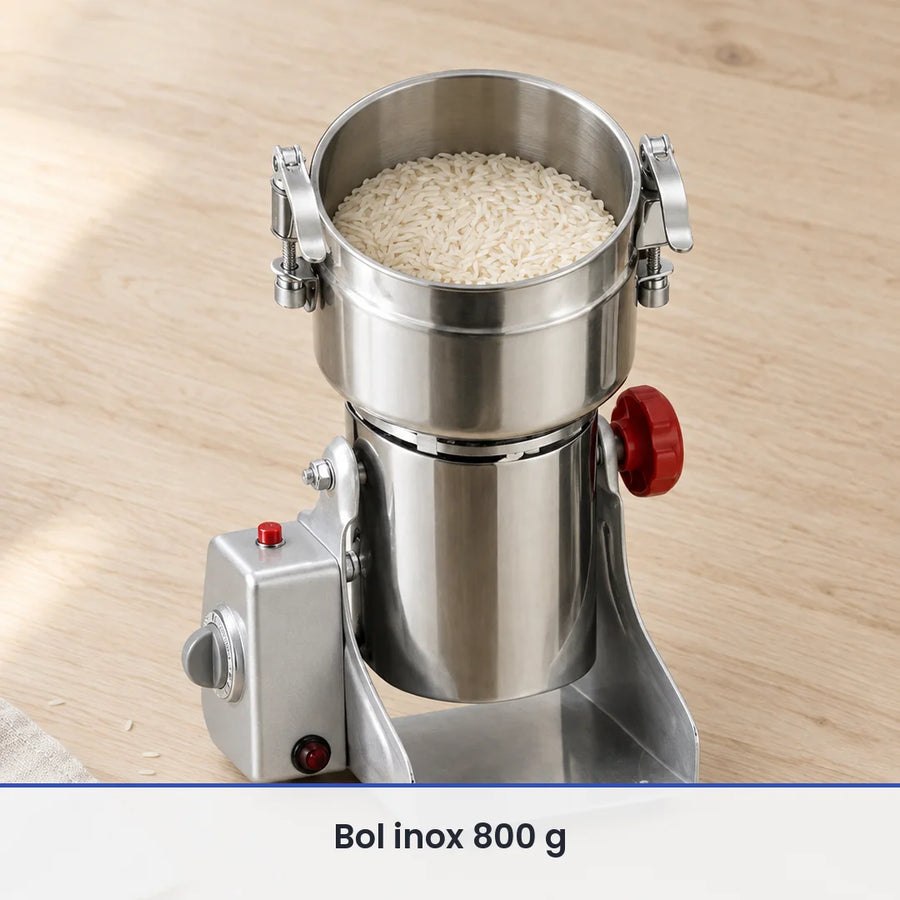 Cuve inox ouverte du moulin électrique 800 g remplie aux deux tiers de grains de riz, sur un plan de travail en bois clair