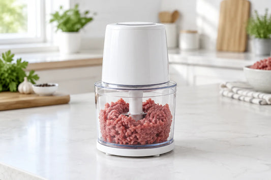 Mini hachoir électrique blanc dont le bol transparent contient de la viande hachée crue