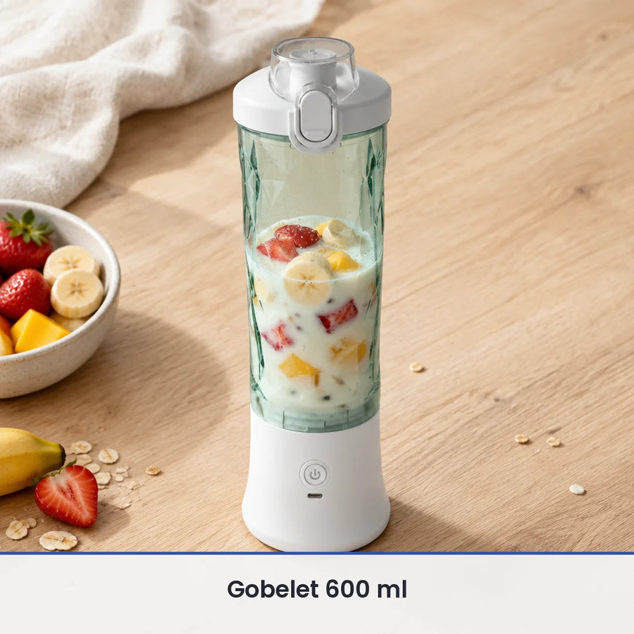 Gobelet vert d'eau du blender portable blanc rempli aux deux tiers de fraises, banane, mangue et lait, sur bois clair