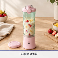 Gobelet vert d'eau du blender portable rose rempli aux deux tiers de fraises, banane et lait, sur une table en bois