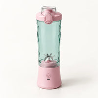 Blender portable 600 ml rose avec gobelet vert d'eau à facettes et couvercle rose à clapet, sur fond blanc cassé