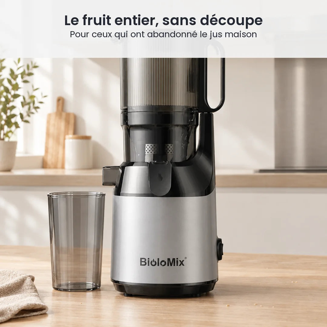 Extracteur de jus BioloMix posé sur le plan de travail d'une cuisine claire, son gobelet à jus transparent fumé à côté