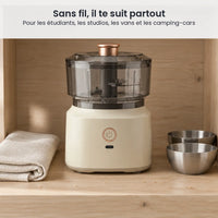 Hachoir électrique sans fil 350 ml beige crème rangé dans un placard en bois clair, à côté d'un torchon et de bols inox