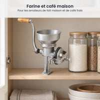 Moulin manuel en fonte argenté rangé sur l'étagère d'un placard de cuisine, à côté de bocaux de farine et de grains