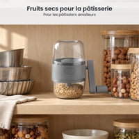 Hachoir à noix gris rangé dans un placard à pâtisserie, à côté de moules et de bocaux de noisettes et de fruits secs