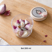 Bol transparent de 200 ml du hachoir rotatif rempli de quartiers d'oignon, couvercle beige rosé posé à côté