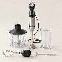 Mixeur plongeant 5 en 1 de 1500 W noir et inox avec bol hachoir, gobelet gradué, fouet et mousseur, sur fond blanc cassé