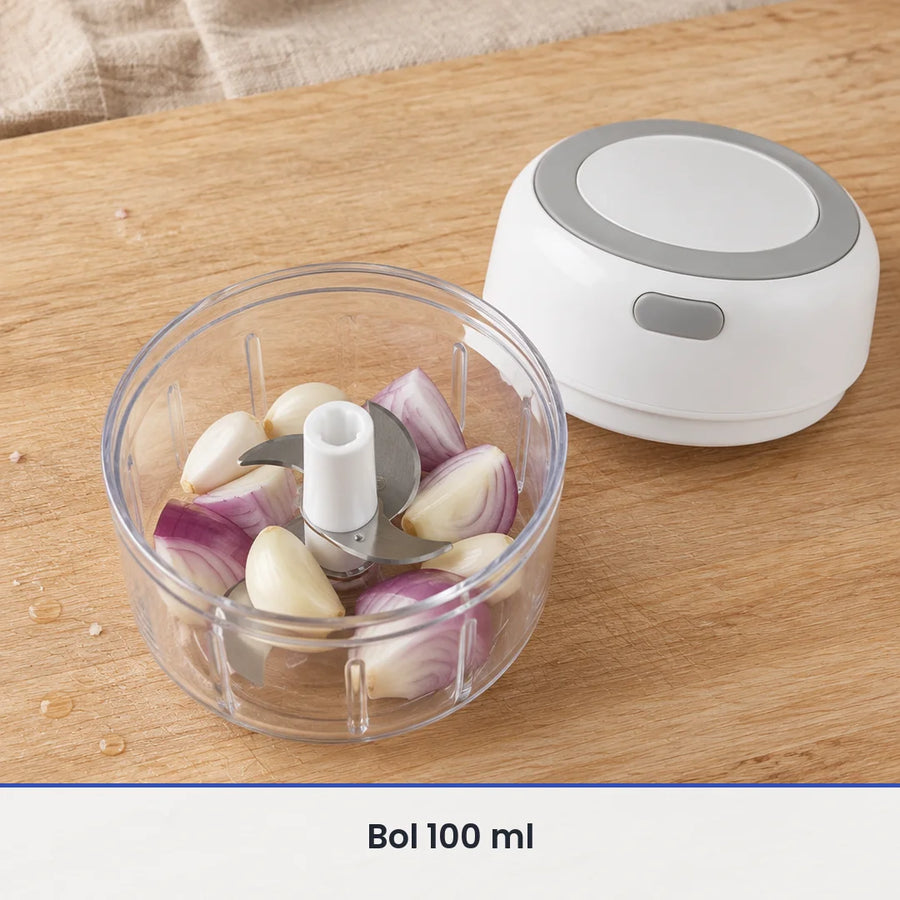 Bol transparent de 100 ml du mini hachoir électrique blanc rempli d'ail et d'oignon rouge, couvercle-moteur posé à côté