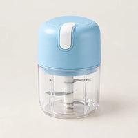 Mini hachoir électrique portable sans fil bleu ciel à bouton blanc, bol transparent et couteau inox, sur fond blanc cassé