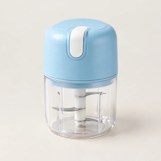 Mini hachoir électrique portable sans fil bleu ciel à bouton blanc, bol transparent et couteau inox, sur fond blanc cassé