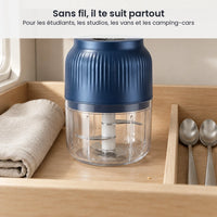 Mini hachoir électrique sans fil bleu marine rangé dans un tiroir de kitchenette en bois clair, à côté d'un torchon