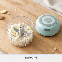 Bol transparent de 100 ml du mini hachoir vert menthe rempli d'oignon et d'ail hachés, couvercle-moteur posé à côté